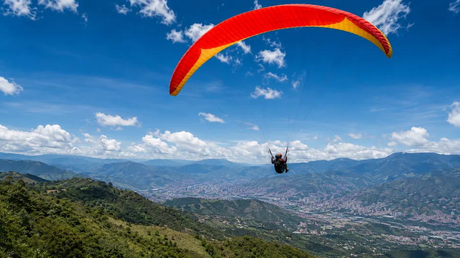 Red and yellow tandem paraglider soaring over the green Aburrá Valley with Medellín spread out below